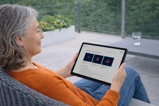 Eine ältere Frau sitzt bequem auf ihrem Balkon und hat auf ihrem Tablet das Sportstättenportal von Groundkeeper geöffnet.